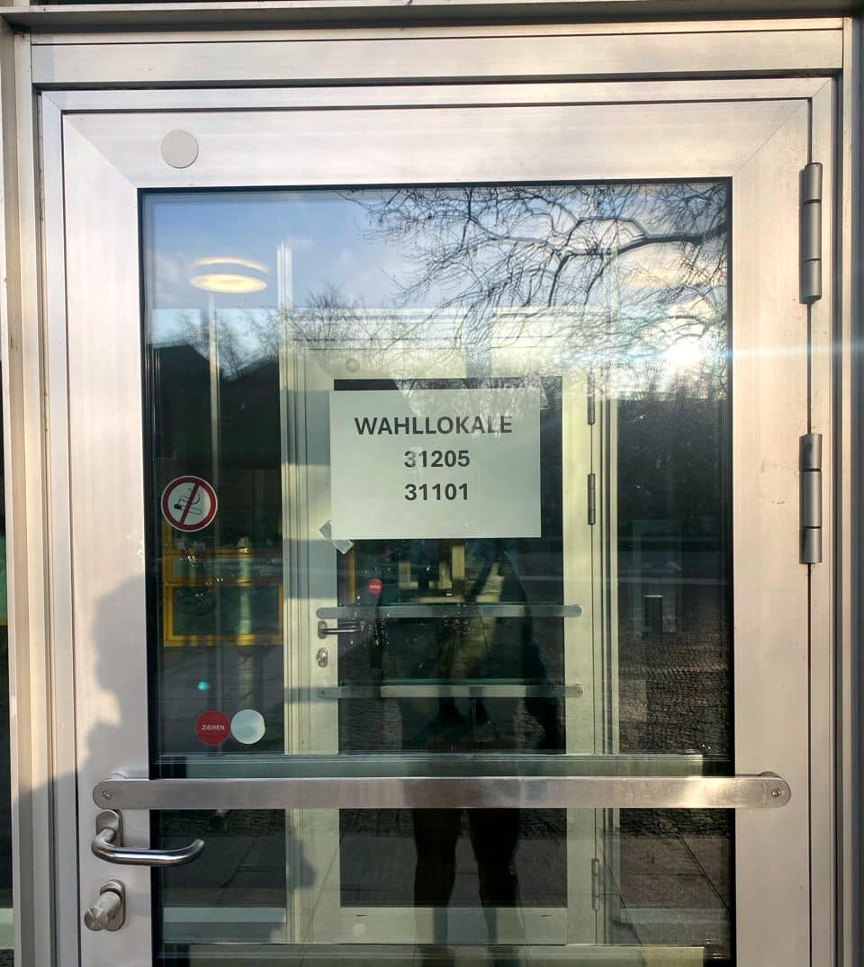 Photo of a metal-and-glass door shining in late afternoon. A piece of paper taped inside says "WAHLLOKALE" (polling place).